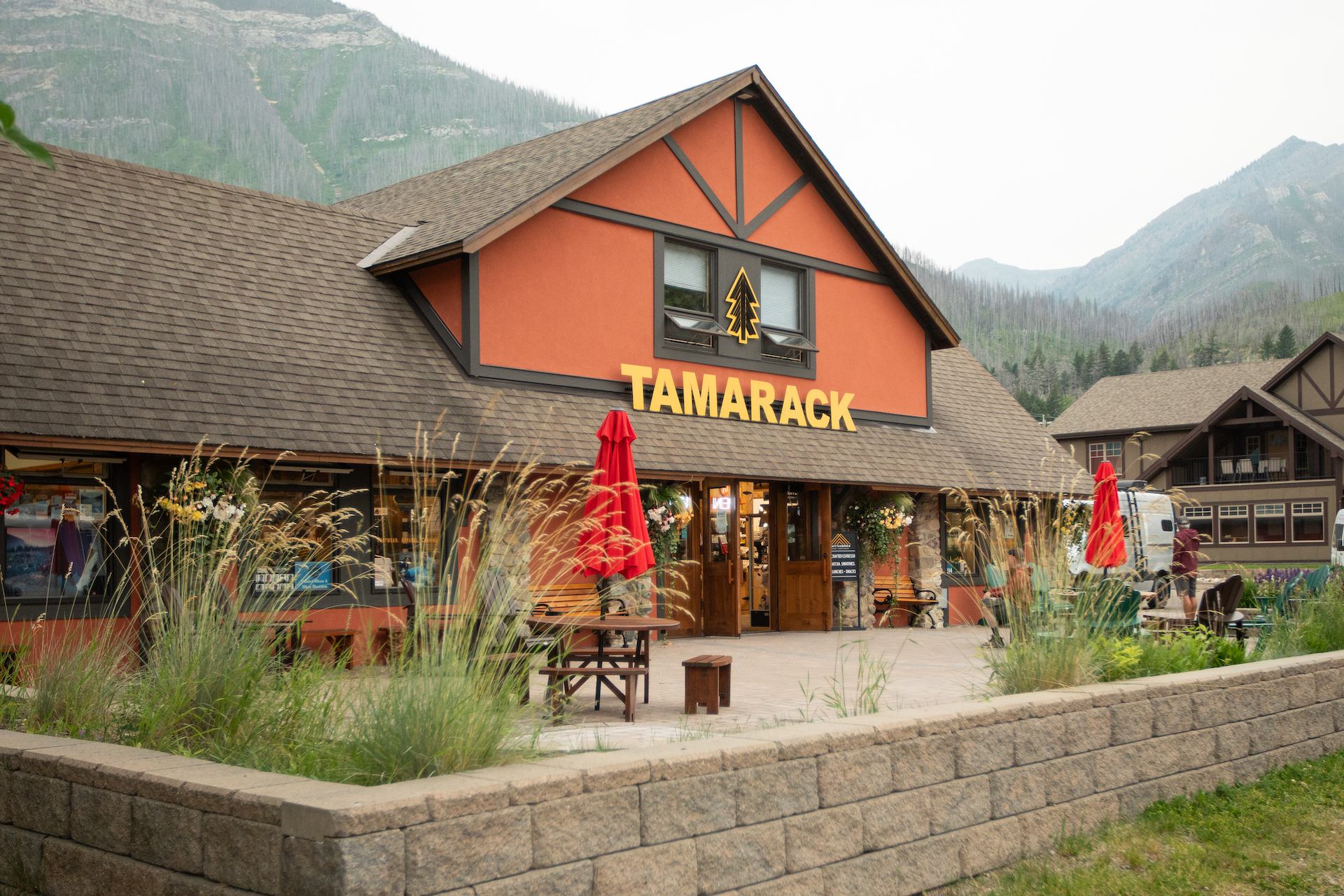 Tamarack building with outdoor seating, red umbrellas, and mountain backdrop.
