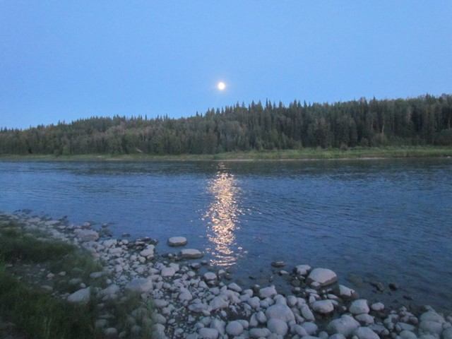 Moonlight on river with rocky shore and forest at Métis Crossing Campground.