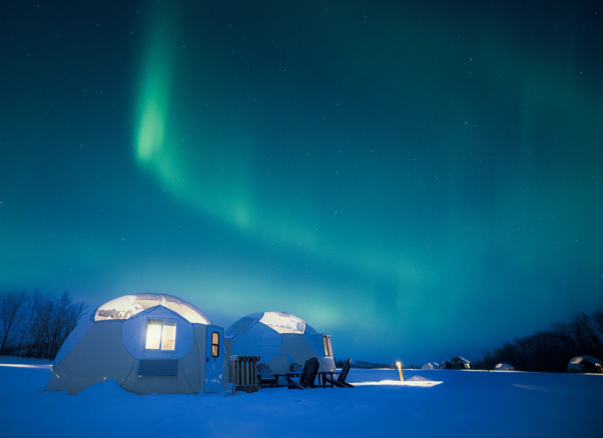 Lit domes under Northern Lights in snowy night at Métis Crossing Sky Watching Domes.