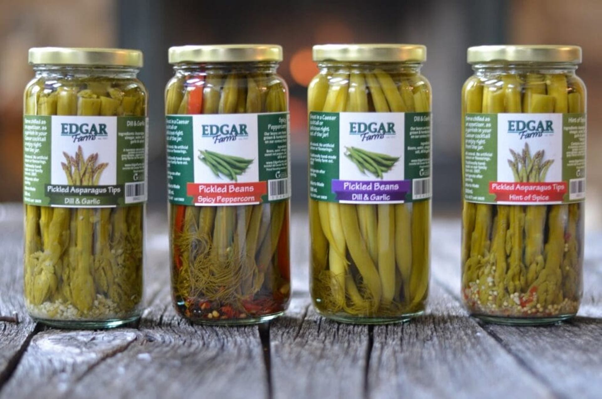 Four Edgar Farms jars of pickled asparagus tips and beans on weathered wood.