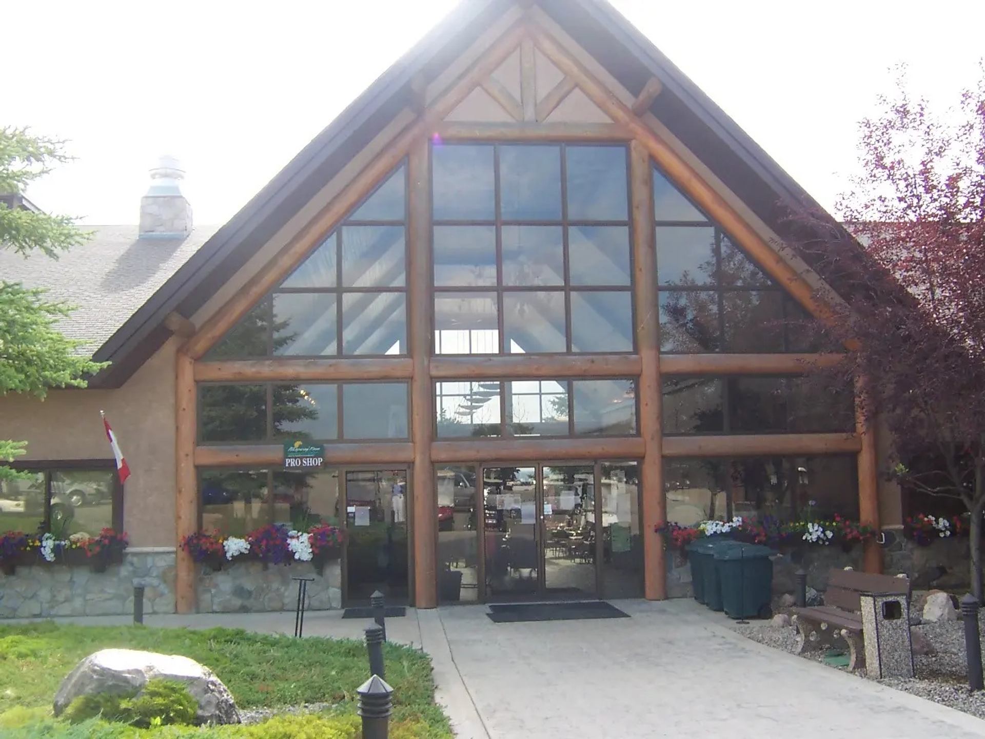 Lodge-style building with large glass entrance, flower boxes, Canadian flag and stone landscaping.