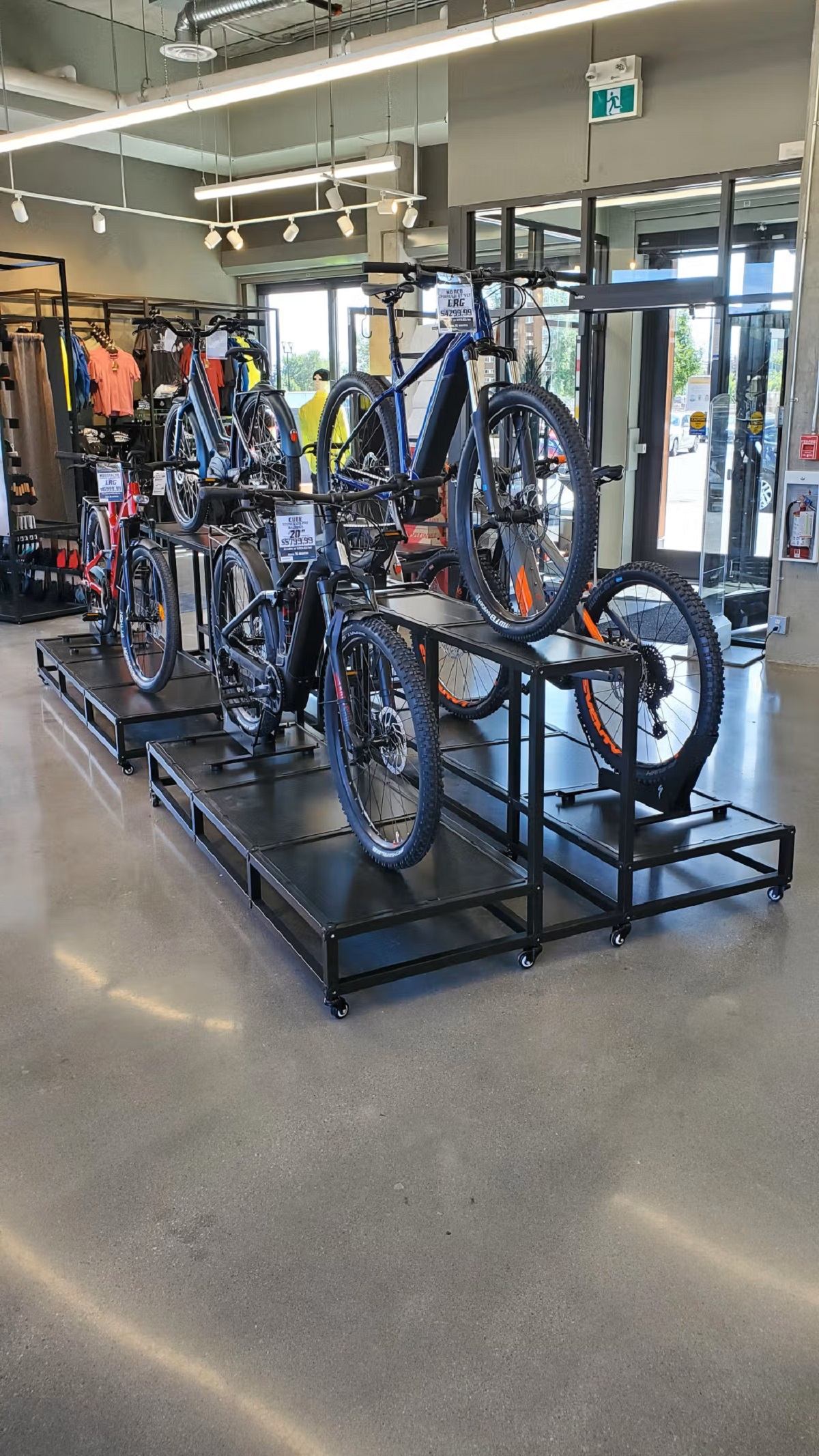 Tiered bike display in modern shop with gear and apparel in the background.