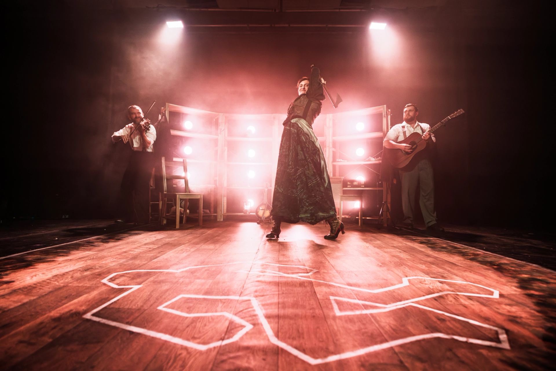 Stage performance with dancer, musicians, bright backlights and chalk body outline on wooden floor.