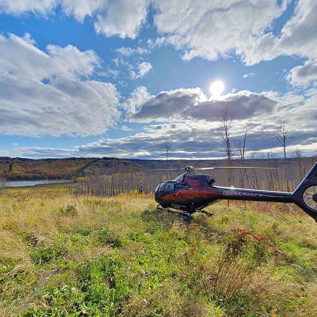 Red helicopter parked on grassy field under a bright blue sky with scattered clouds.