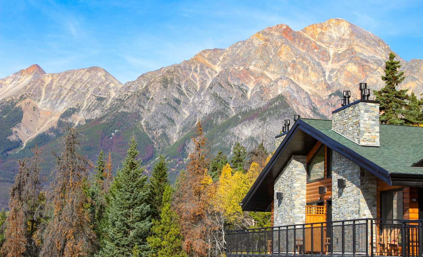 The upper floor of a lodge unit with large trees and mountains in the background below a blue sky.