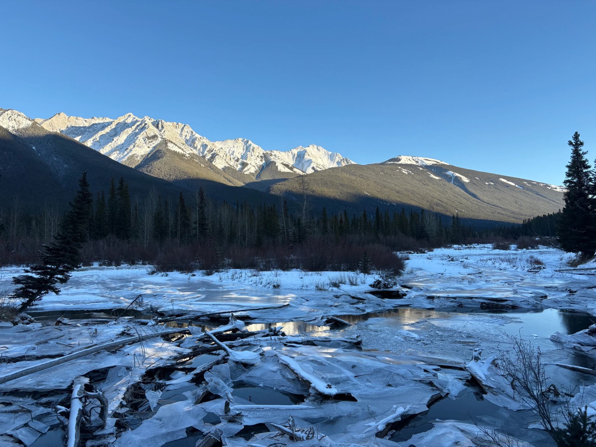Snow‑covered mountains above a frozen, cracked river in a quiet valley.