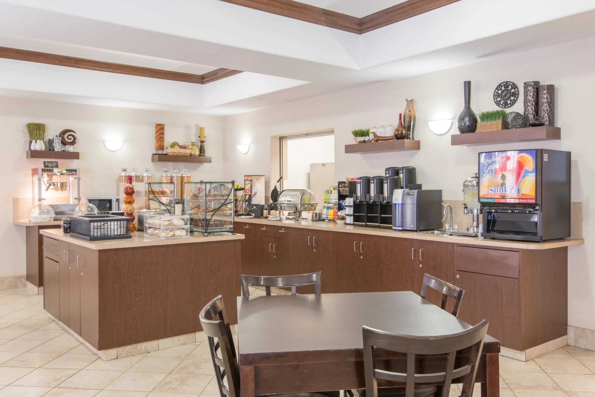 Hotel breakfast area with buffet counters, drink machines, pastries and seating table.