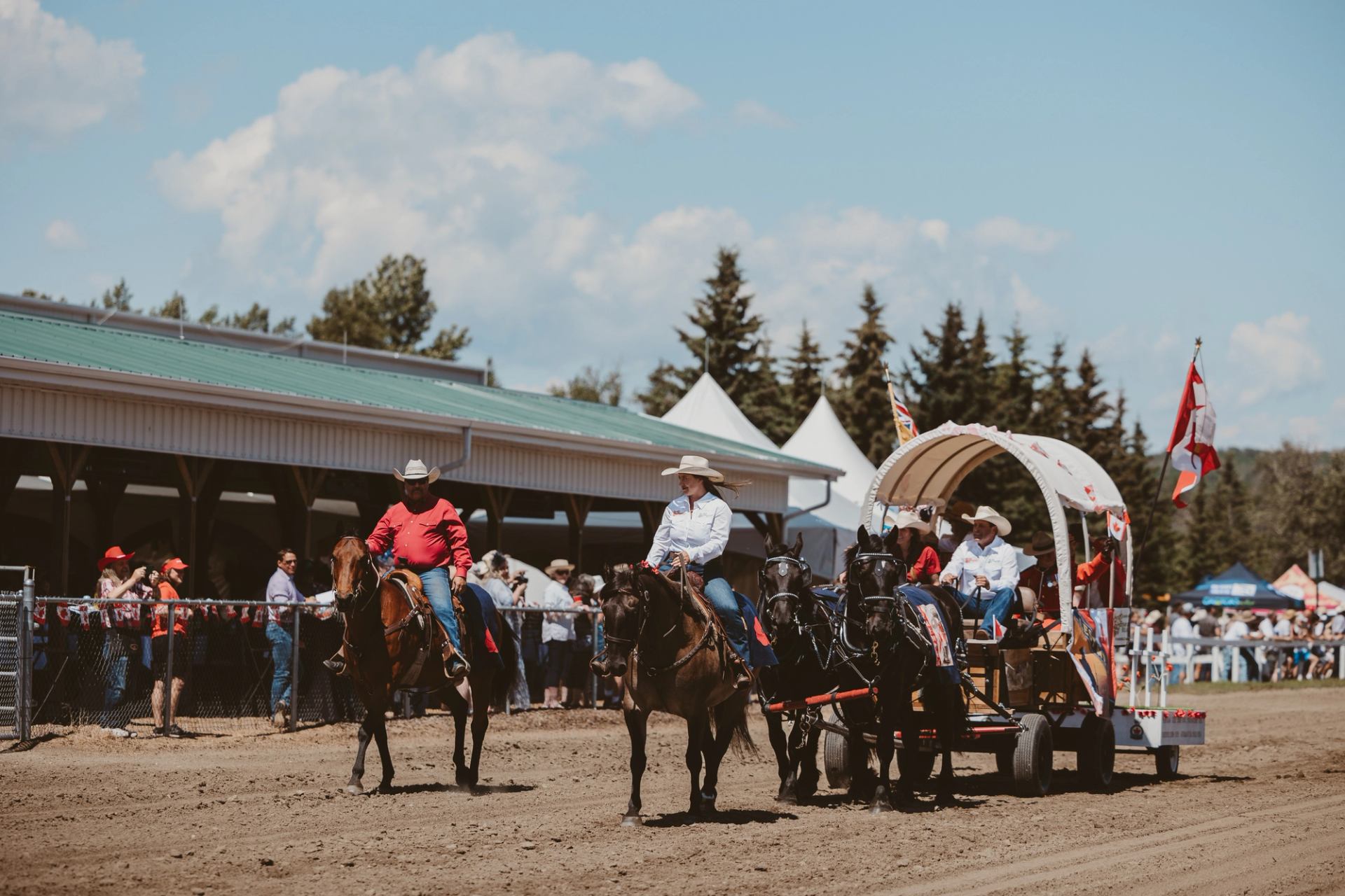 Riders on horseback and a covered wagon move along a dirt arena during a traditional event at Millarville.