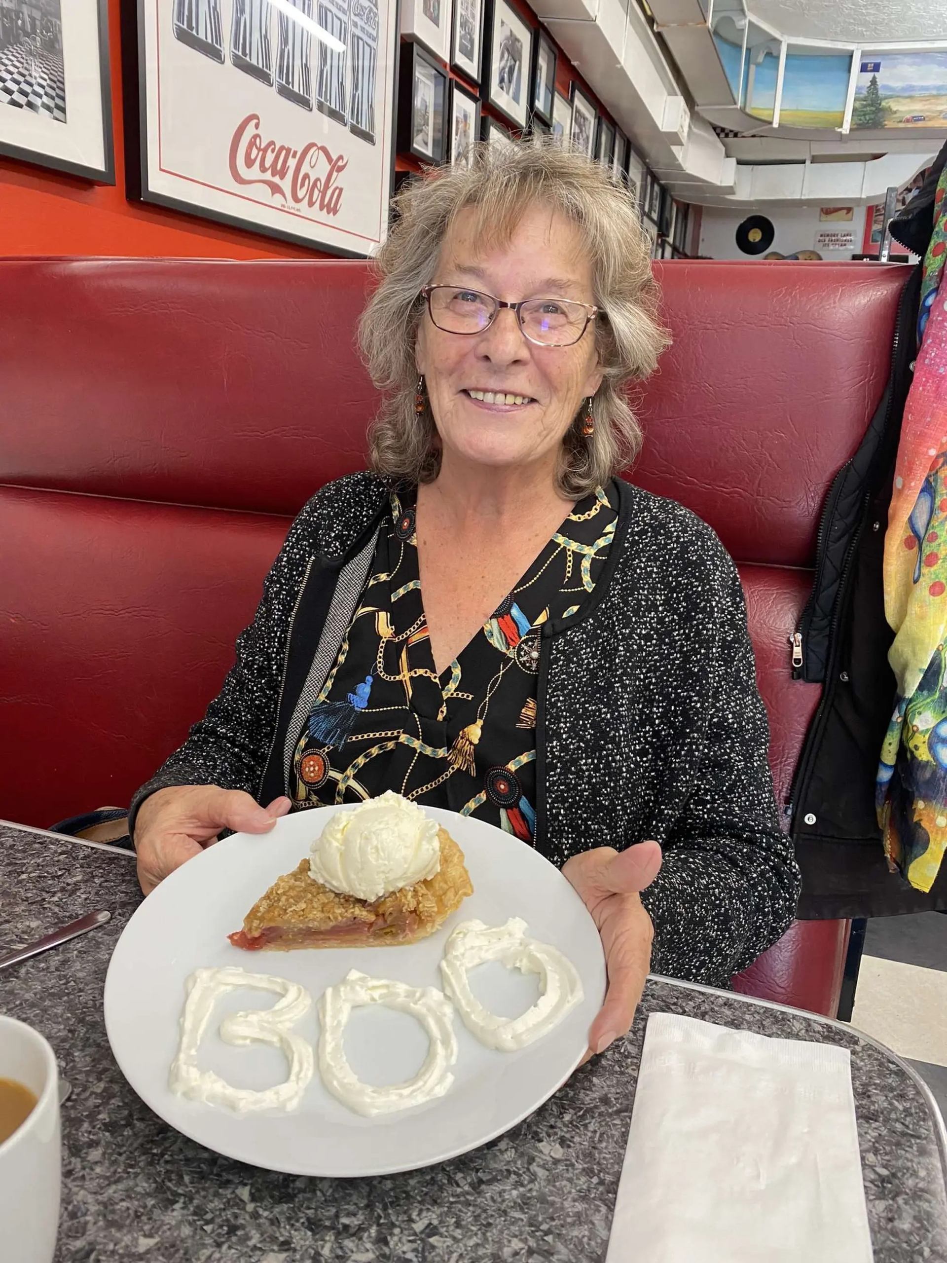 Person in diner booth holding pie with ice cream and whipped cream spelling BOO.