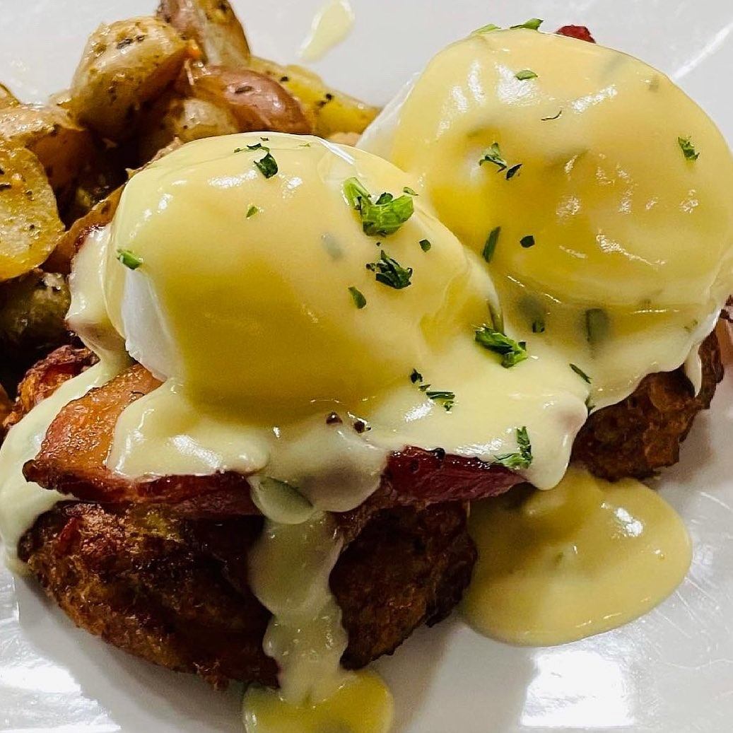 Poached eggs with hollandaise on toasted bread, served with roasted potatoes.