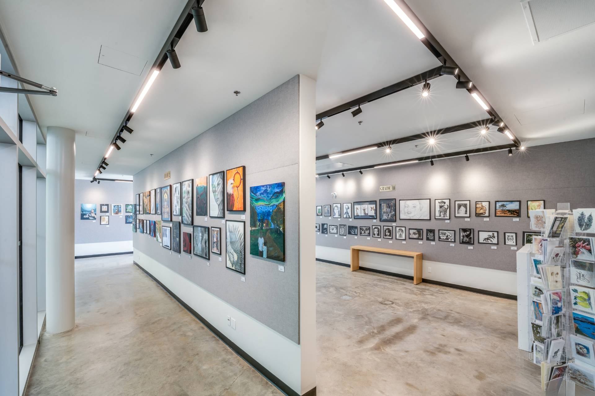 Contemporary gallery hallway with framed artworks on grey walls and track lighting overhead.