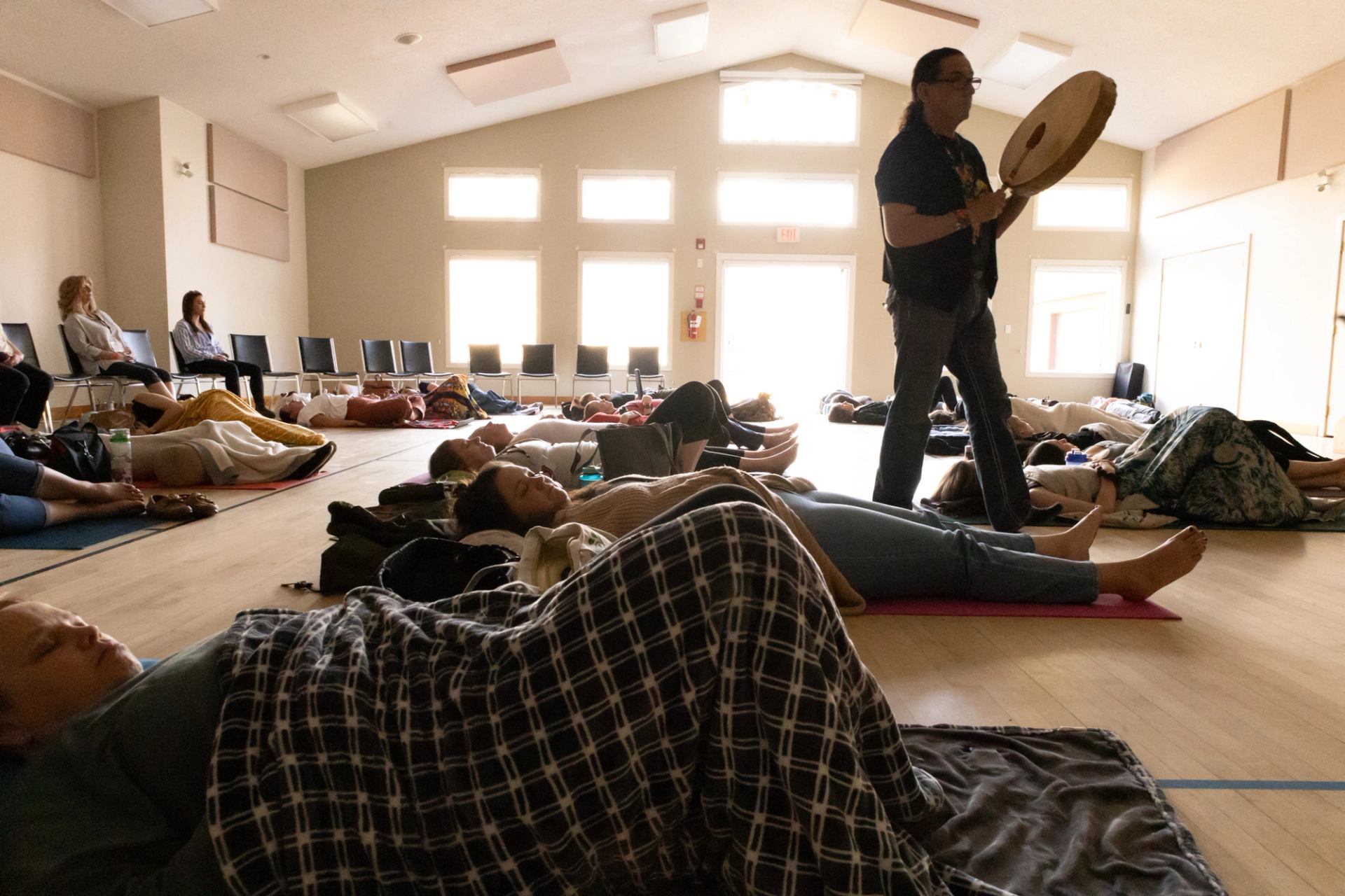 Community hall scene with people lying on mats while a person plays a hand drum.