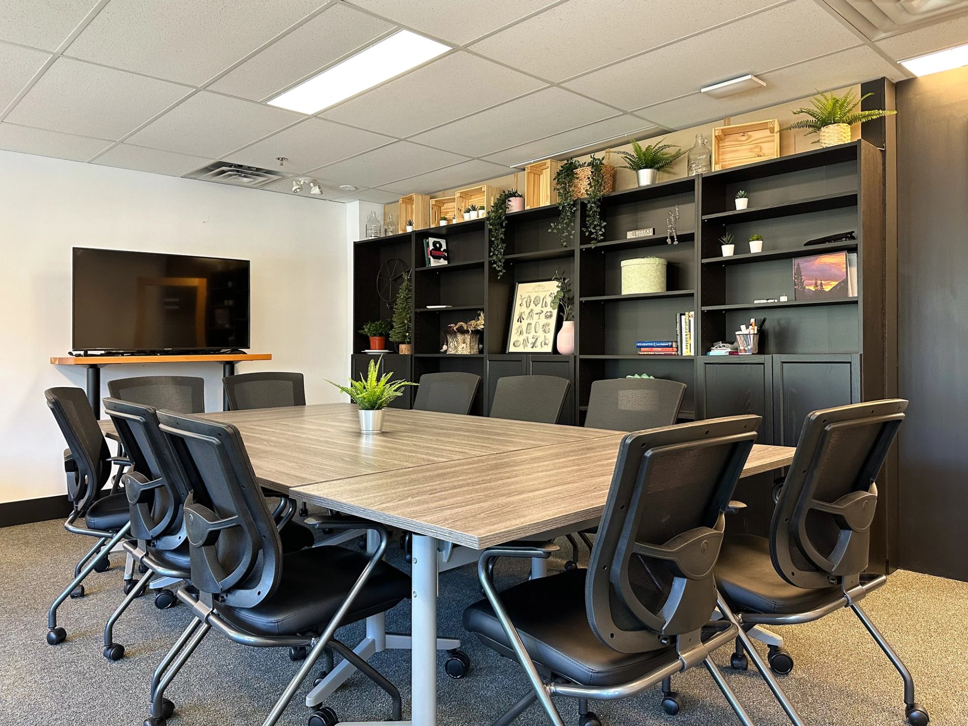 Bright and airy meeting room set up with a large rectangle table, comfortable chairs, and smart TV.