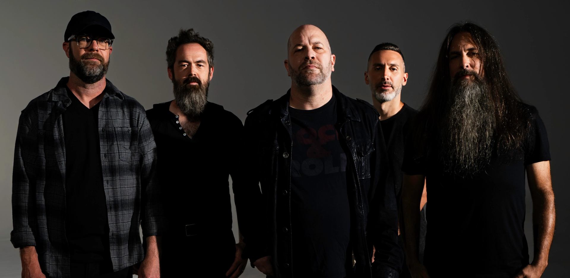 Five band members stand in a row against a plain dark studio background.
