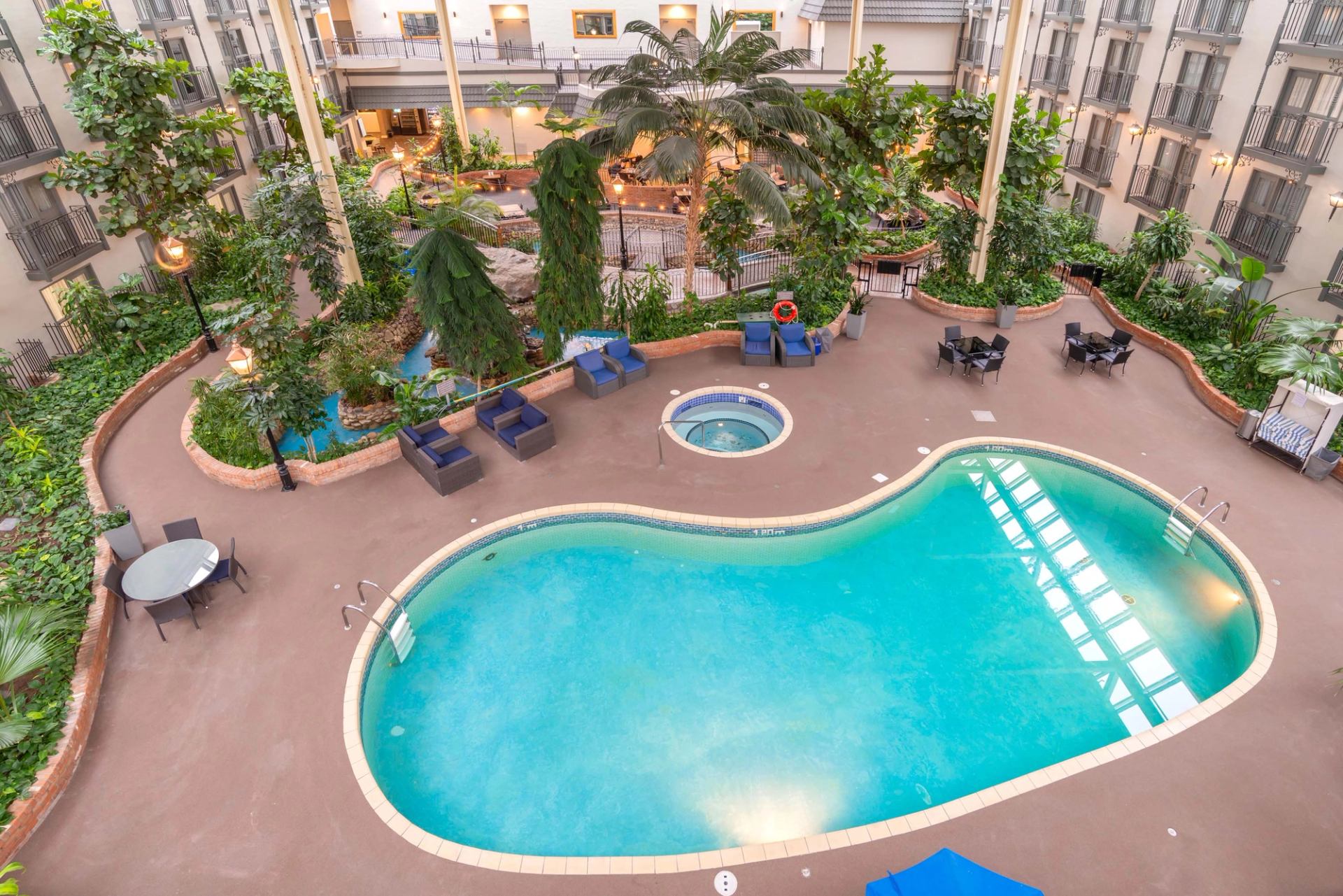 Indoor hotel courtyard with pool, hot tub, lounge chairs and surrounding tropical plants.