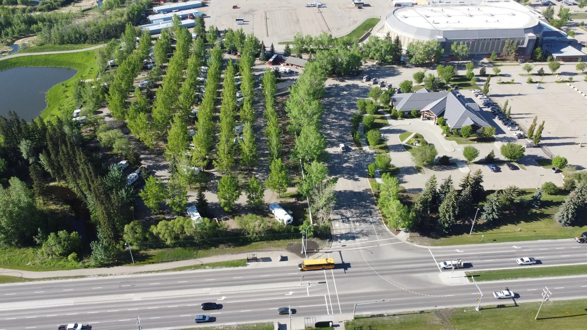 Aerial view of park with trees, buildings, and a busy road with vehicles.