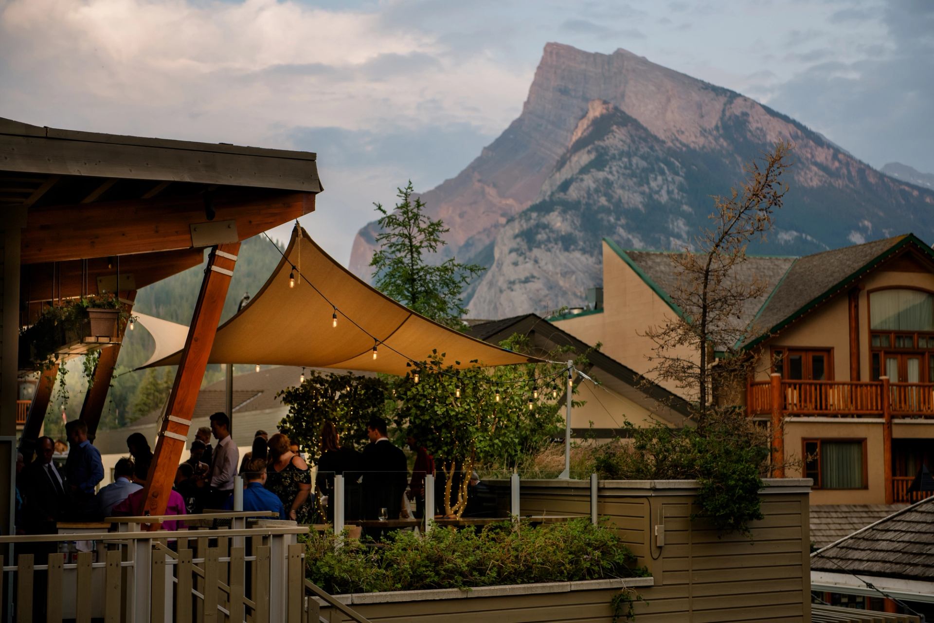 People gather on an outdoor patio under a fabric canopy with string lights.