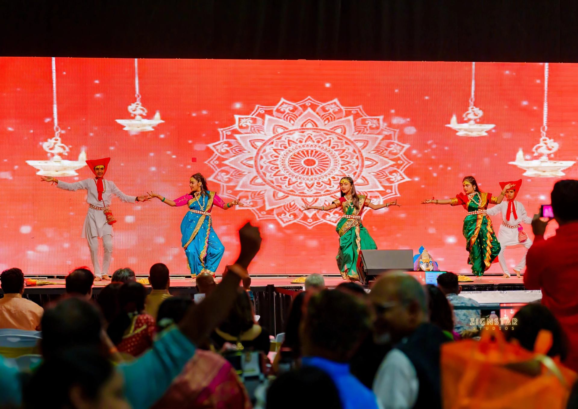 Dancers in colourful traditional clothing perform onstage before a seated audience.