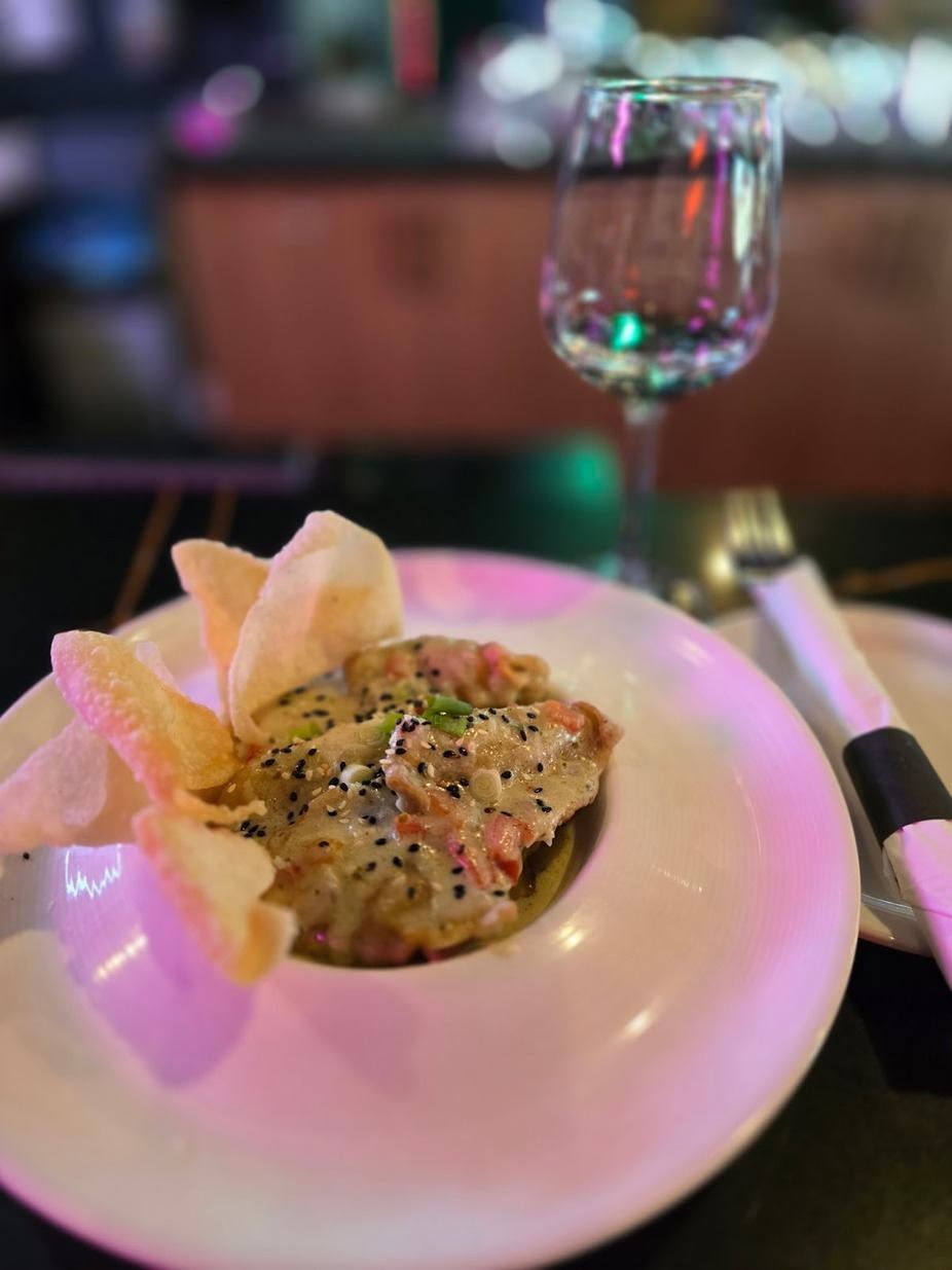 Plated chicken dish with chips on a white plate, beside a wine glass.