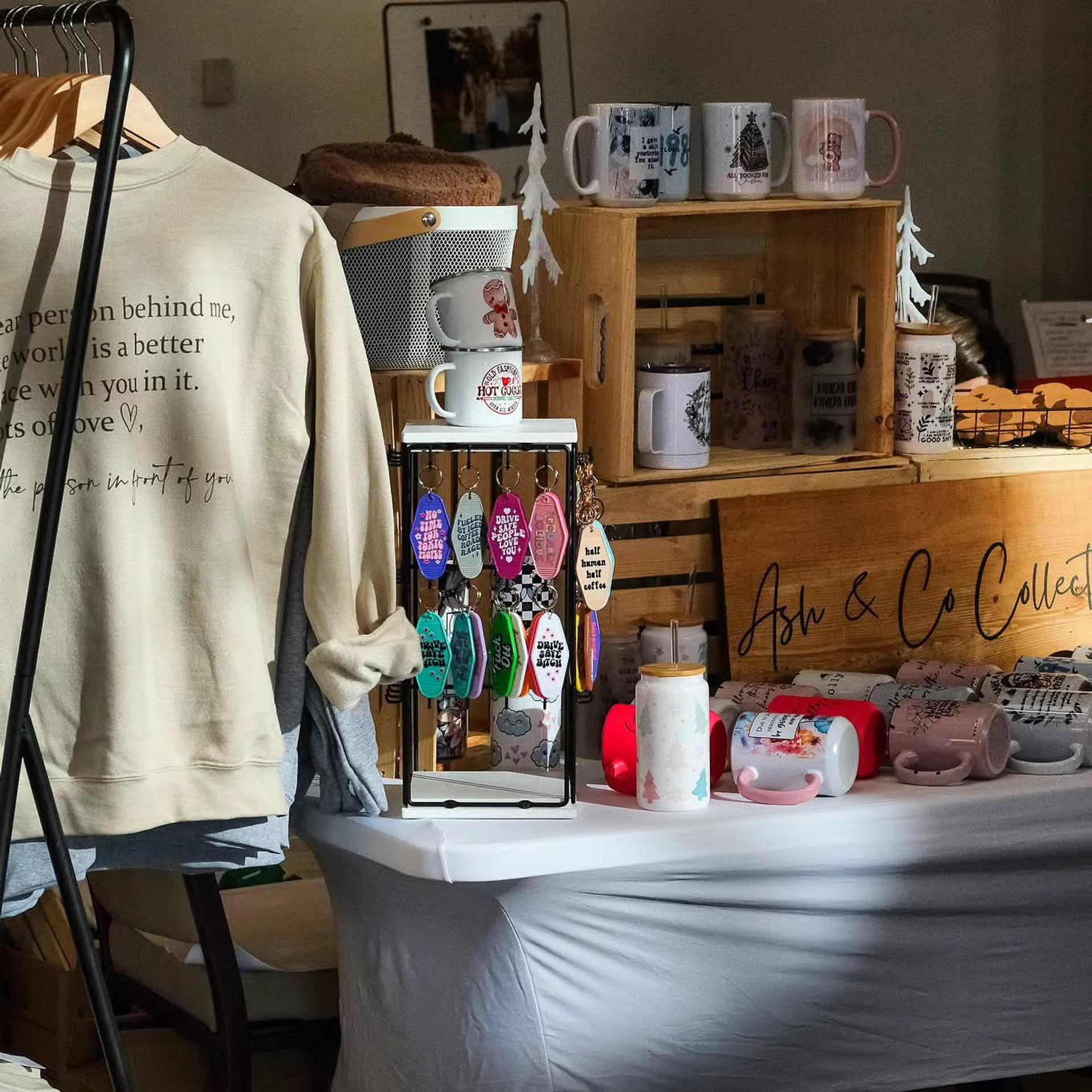 Craft booth with sweatshirt, colorful keychains, mugs, and handmade decor items.