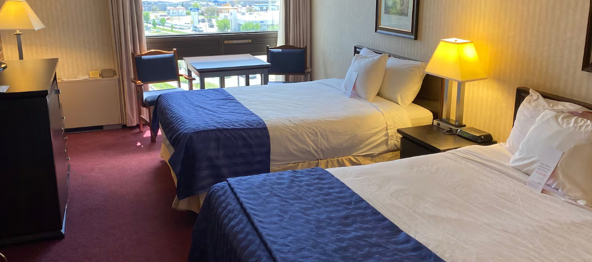 Hotel room with two beds, table, chairs, and large window view.