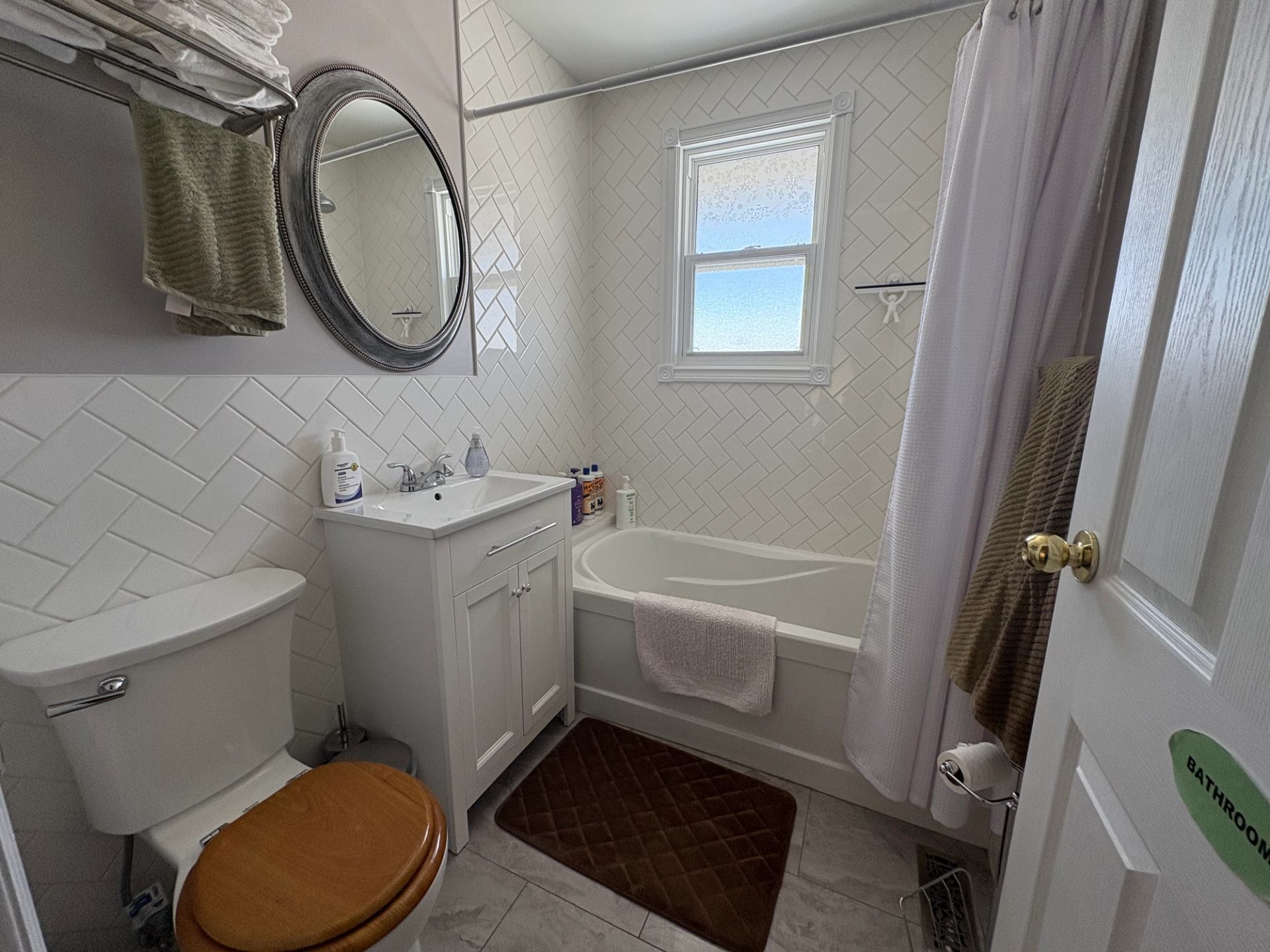 Small bathroom with bathtub, white tiles, vanity sink, toilet and hanging towels.