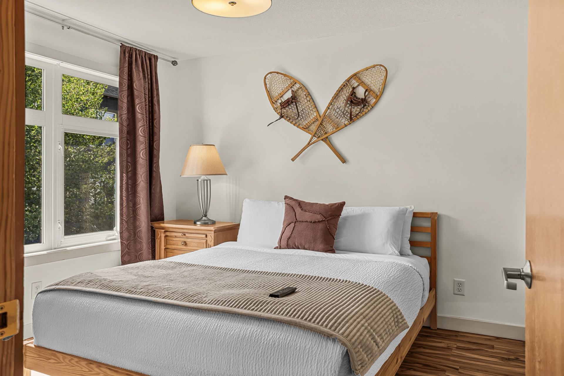 Bedroom with wooden bed, bedside lamp, large window and crossed snowshoes on wall.