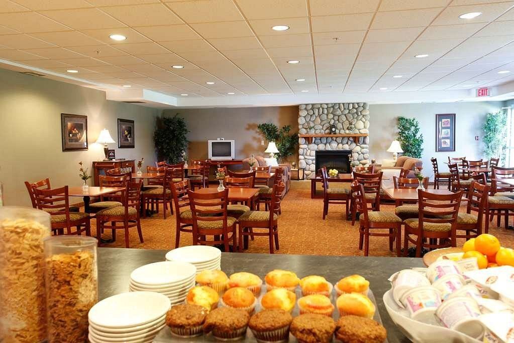 Breakfast area with tables, chairs, and a counter displaying muffins, cereal, and fruit.