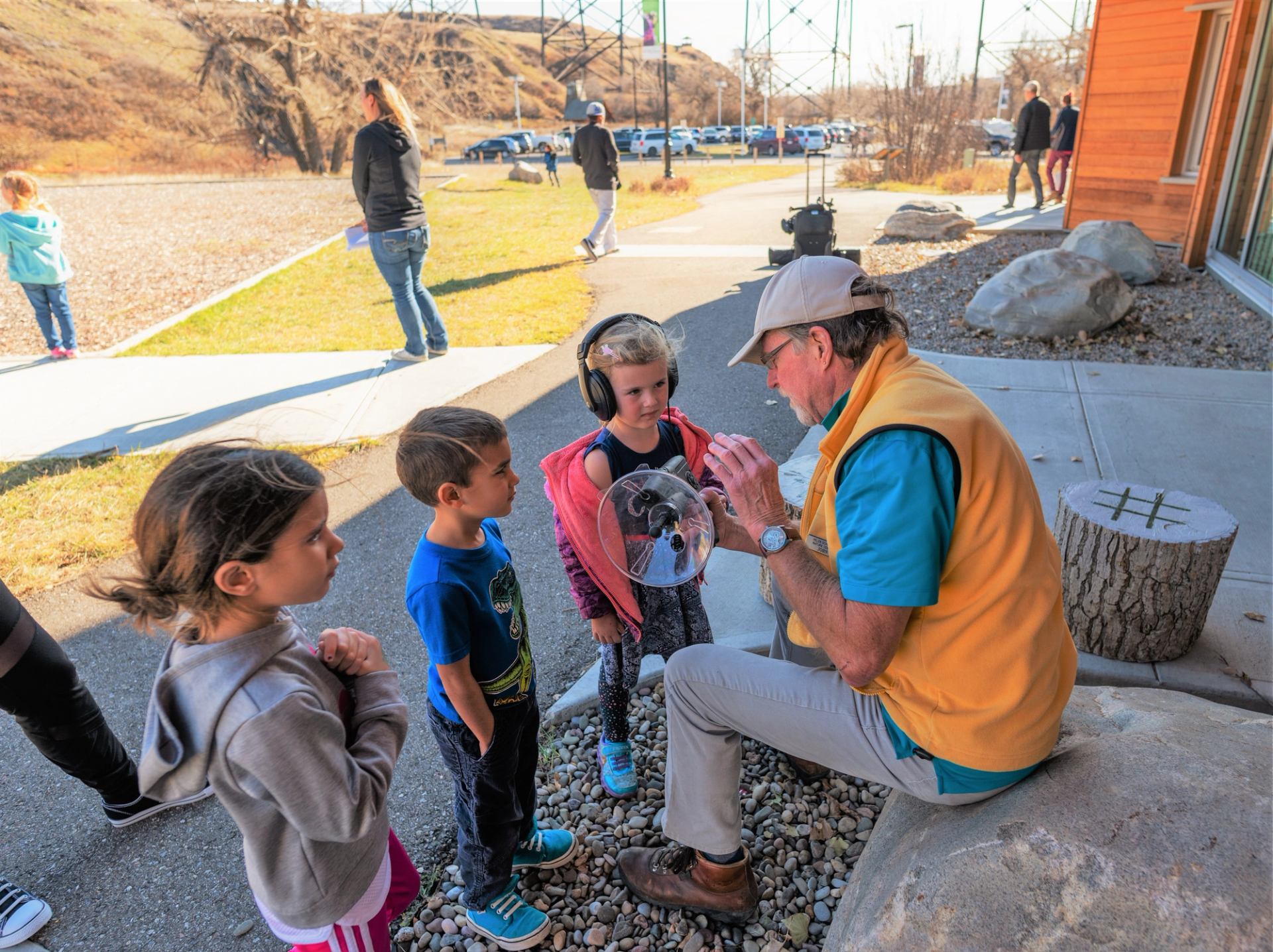 A group of children listens to an instructor showing a nature demonstration outside.