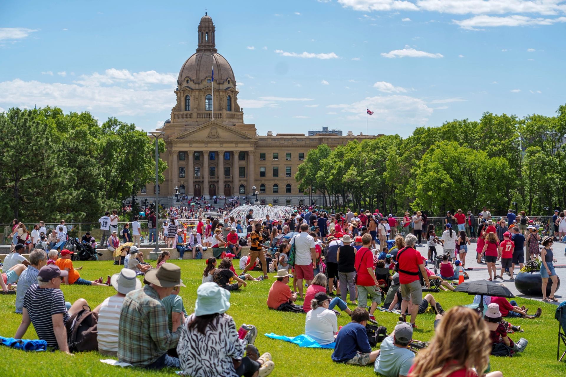Crowd gathers on lawn in front of domed government building and fountain.