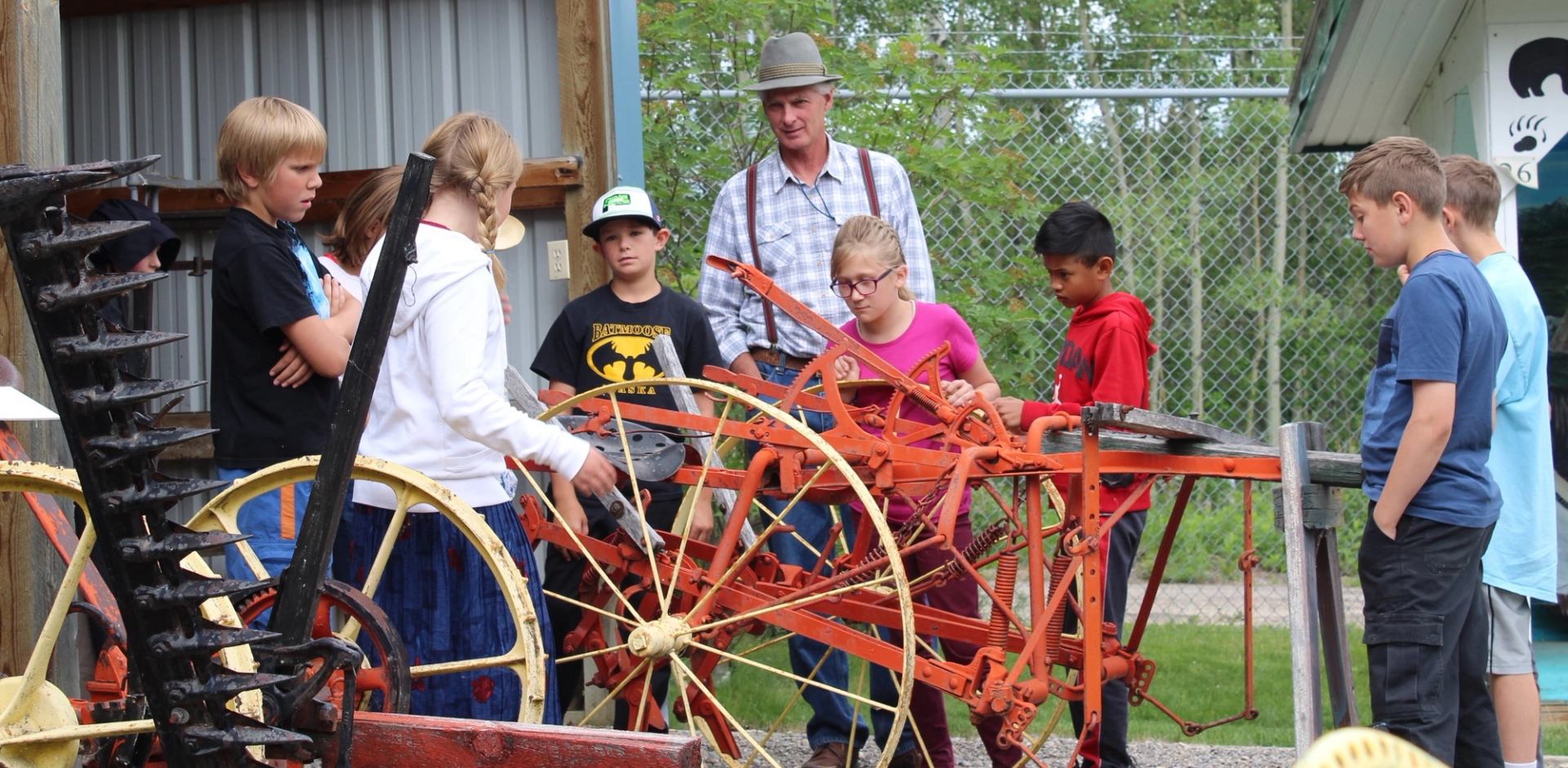 An adult teaches a group of children about vintage farm machinery.