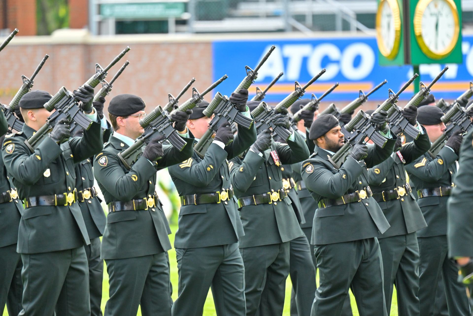 Uniformed guards raise rifles in a coordinated ceremonial salute on the field.