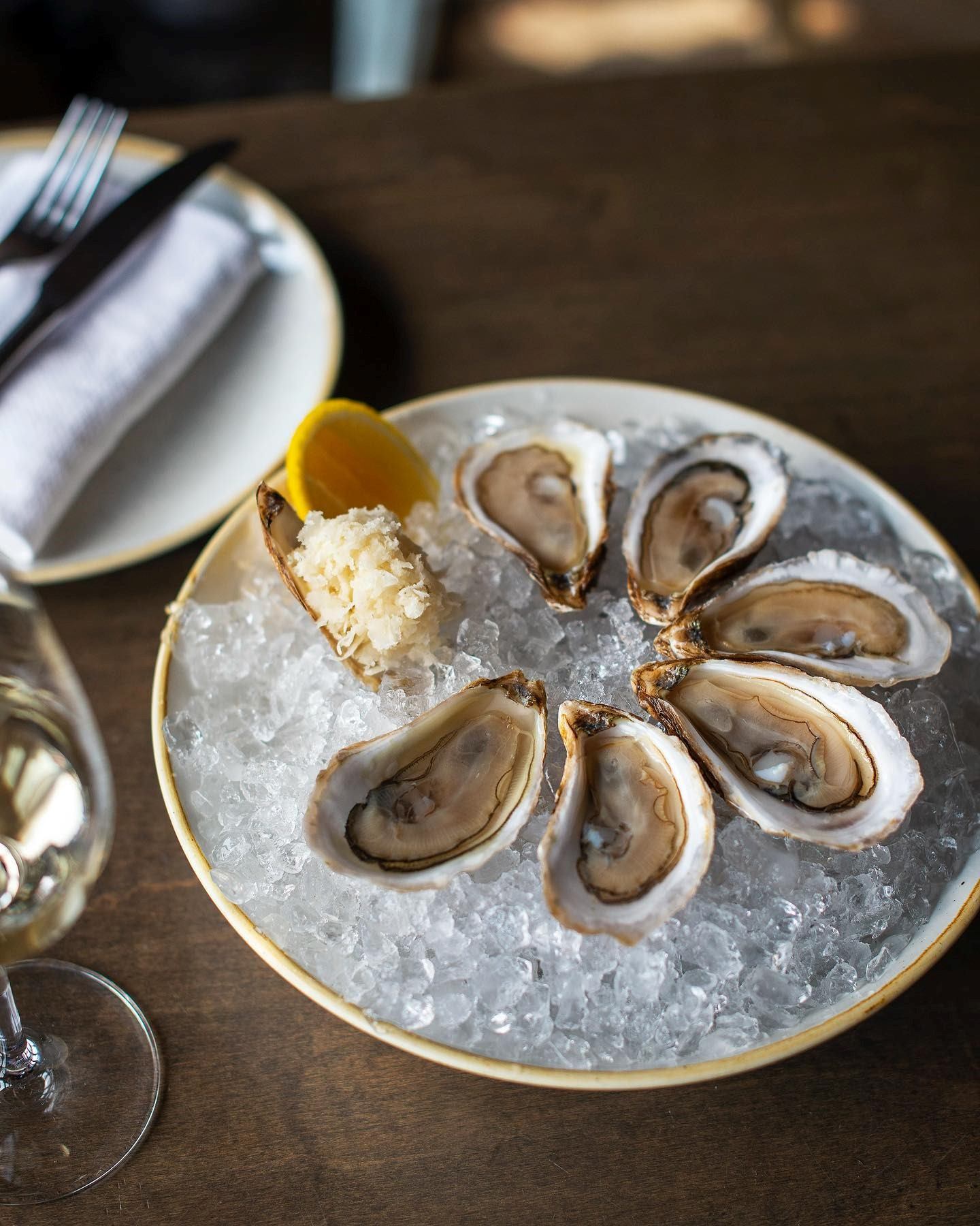 Model Milk oysters on ice with lemon, horseradish, and a glass of white wine.