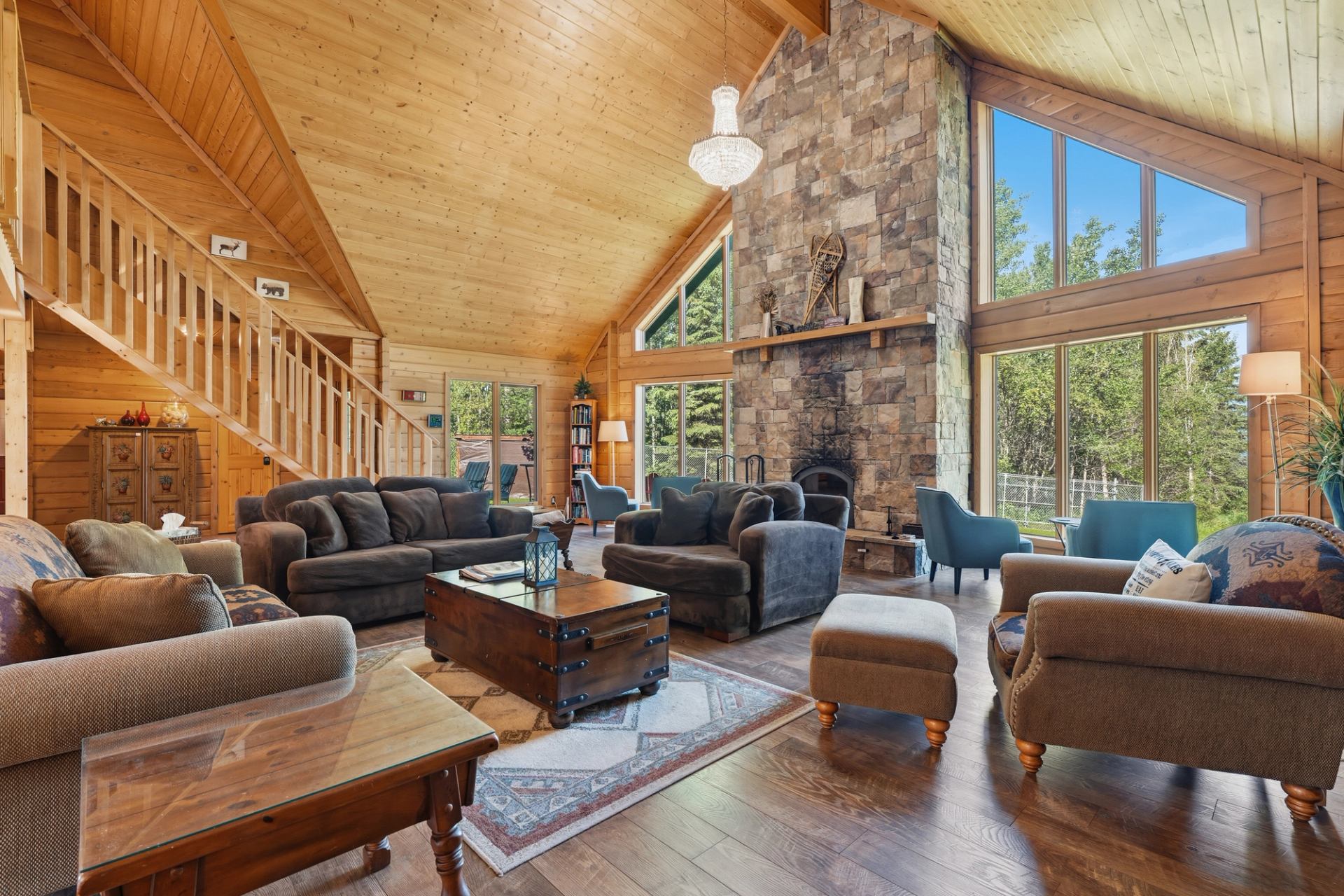 Wood-panelled living room with stone fireplace, large windows, sofas and armchairs.