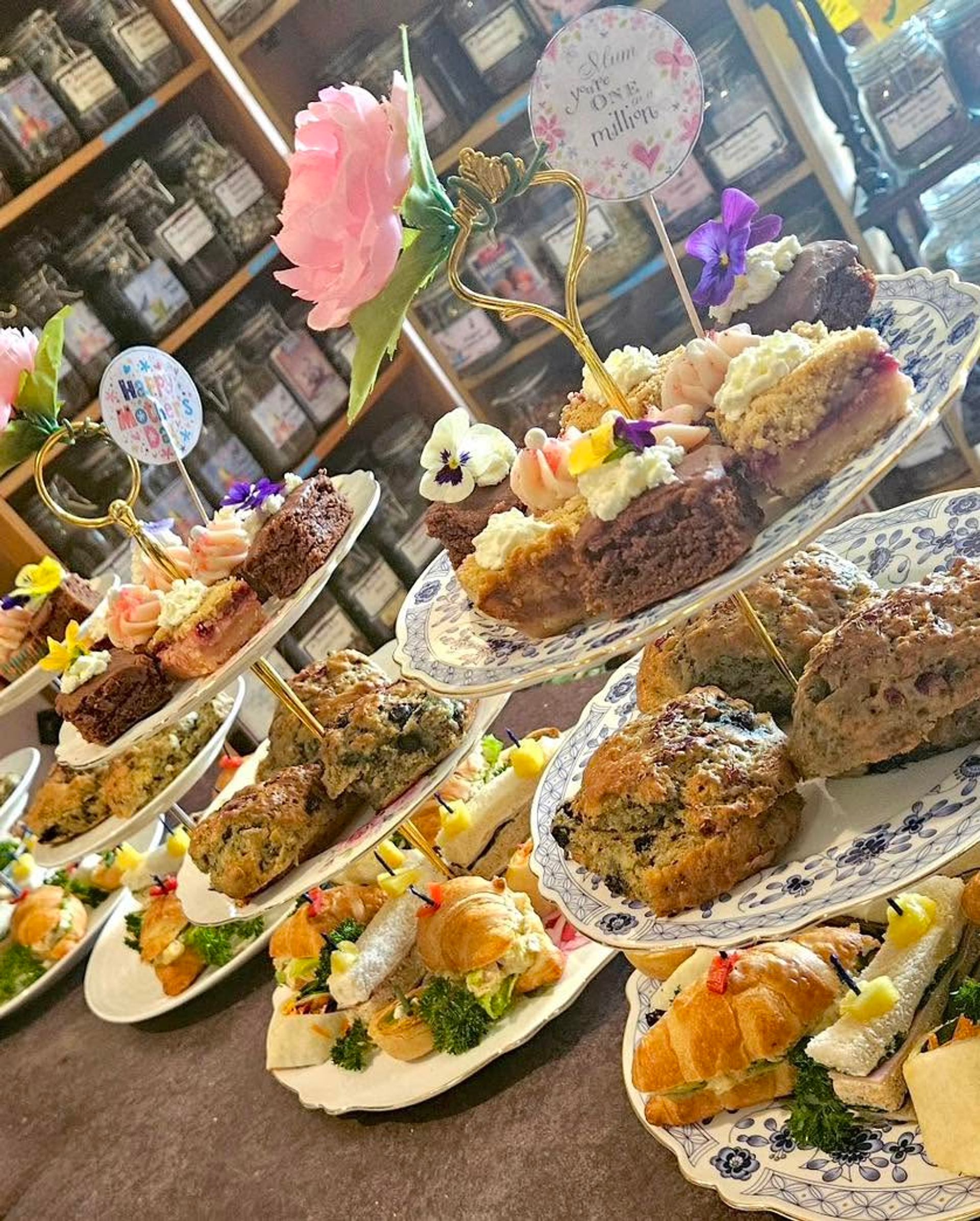 Tiered trays display scones, pastries, sandwiches, and garnishes in a tea room setting.