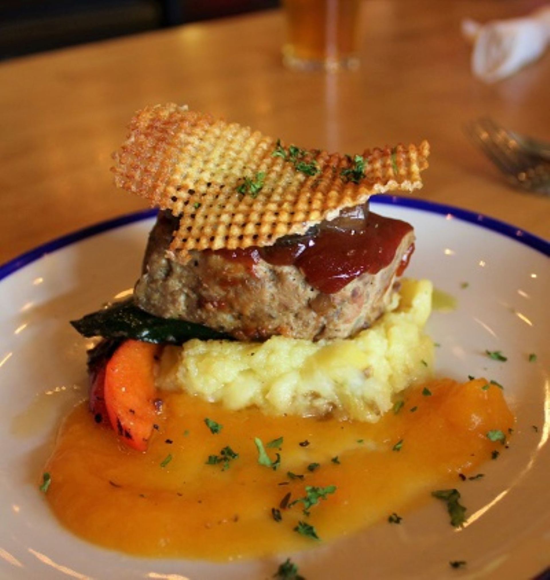 Plated gourmet dish with meat, mashed potatoes, vegetables, and rich sauce on a restaurant table.