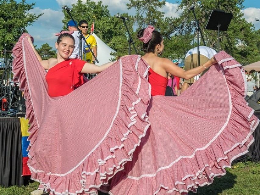 Dancers in red dresses perform with pink shawls at Edmonton Heritage Festival stage event.