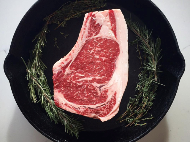 Raw ribeye steak in cast-iron skillet with sprigs of rosemary and thyme.