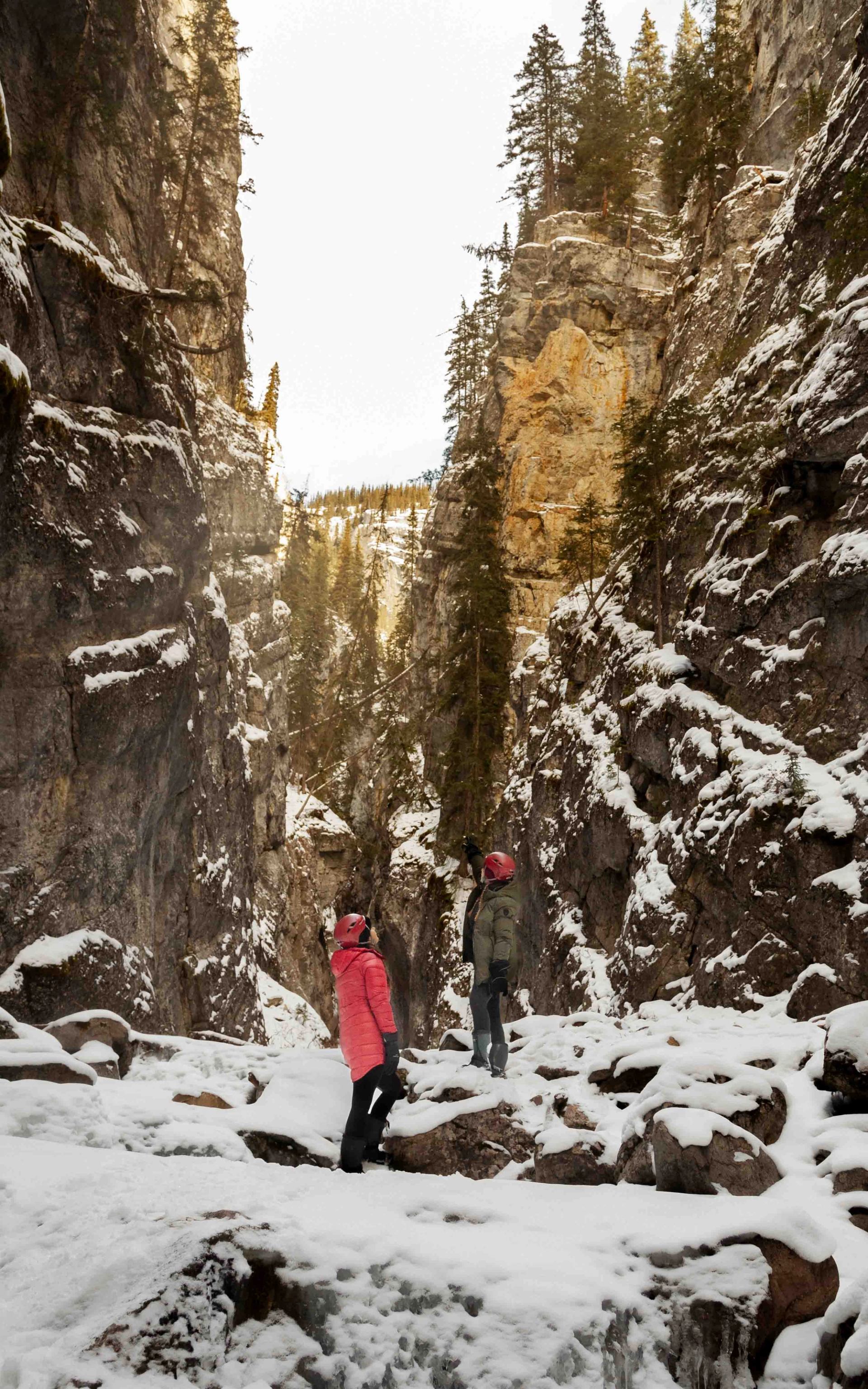 Two people standing on icy ground surrounded by towering canyon cliffs