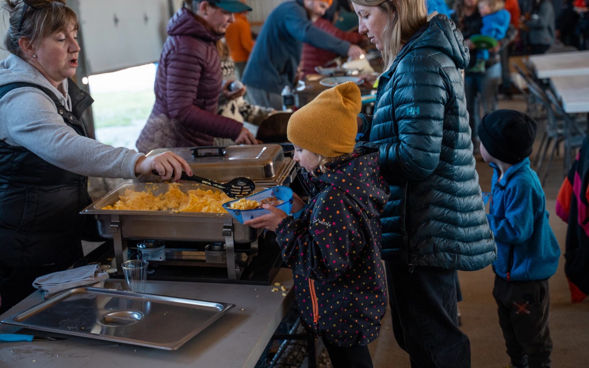 People serving food from chafing dishes during a group meal indoors.