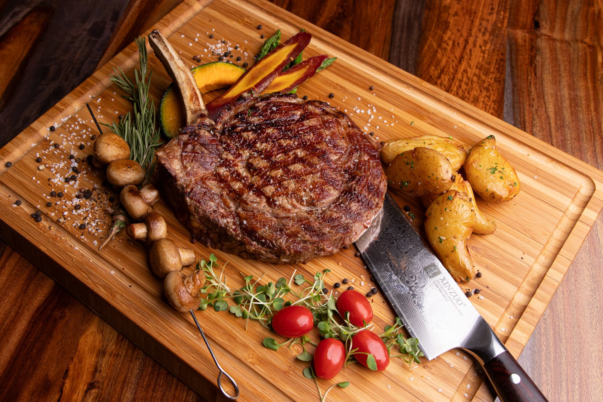 Grilled bone-in steak with potatoes, mushrooms, vegetables and a knife on a wooden board.