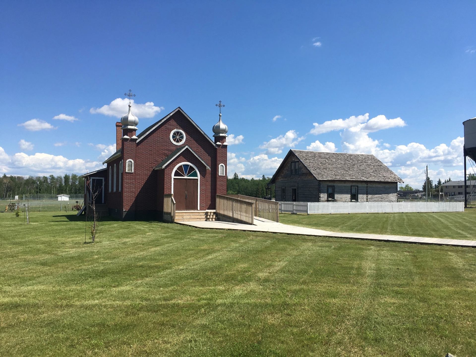 Historic red church and log building on green grounds at Nampa and District Museum.