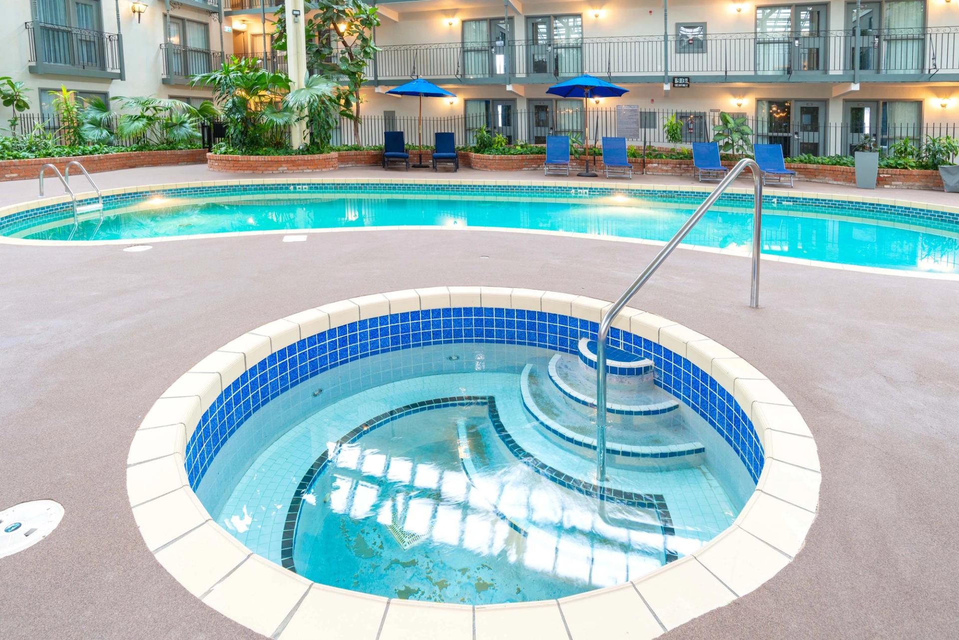 Indoor hotel courtyard with round hot tub, swimming pool, lounge chairs and blue umbrellas.