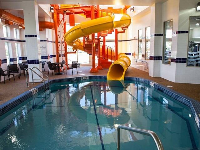 Indoor swimming pool with yellow spiral waterslide, seating area and tiled columns.