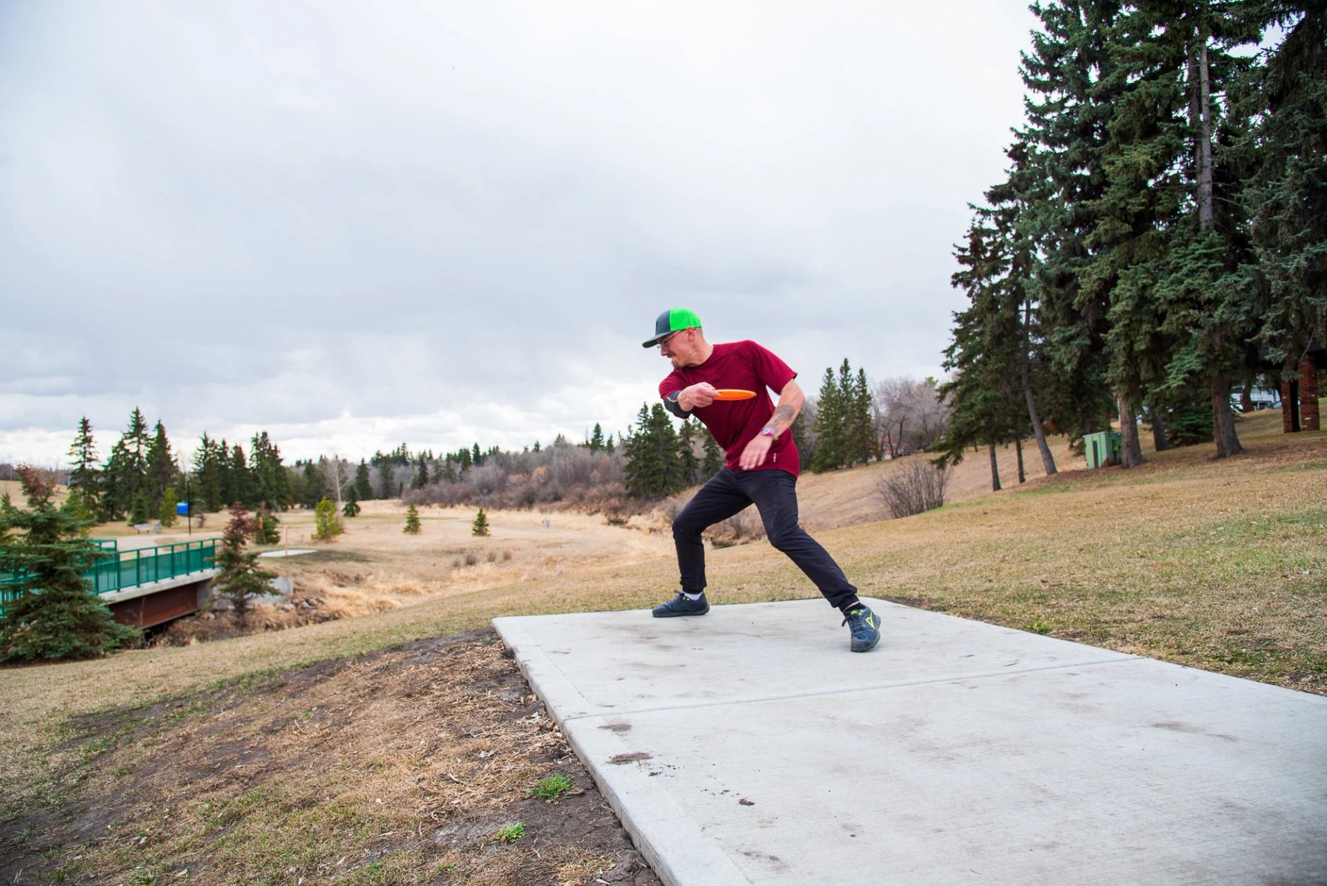 A young adult winding up to throw a disc from the concrete tee pad on hole 1 of the Stoney Creek Disc Golf Course.