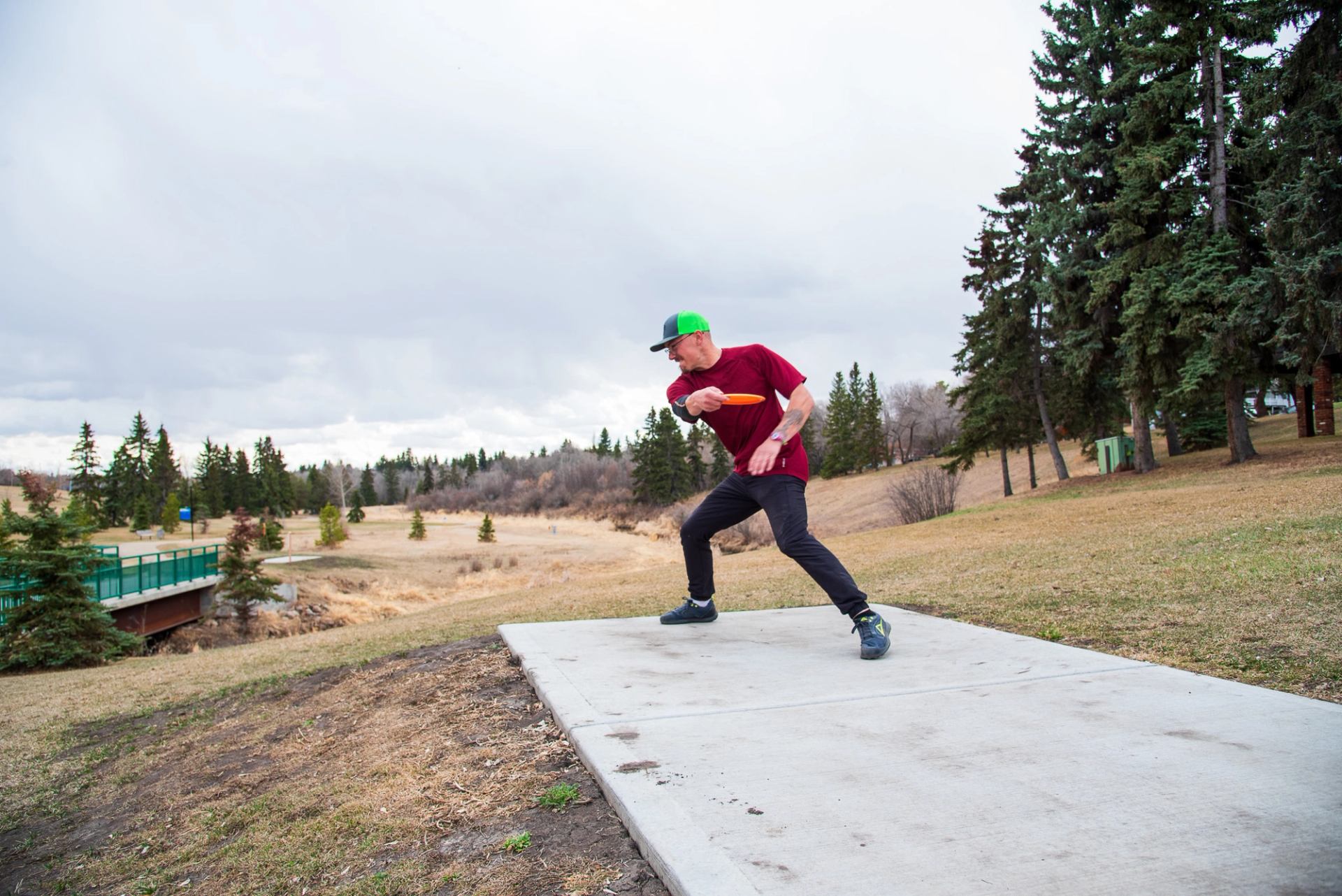 A young adult winding up to throw a disc from the concrete tee pad on hole 1 of the Stoney Creek Disc Golf Course.
