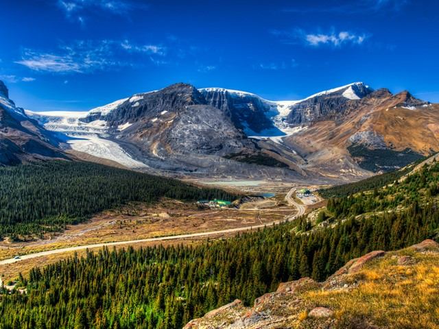 Mountain valley landscape with glacier, winding road, forest and rocky slopes in Banff National Park.