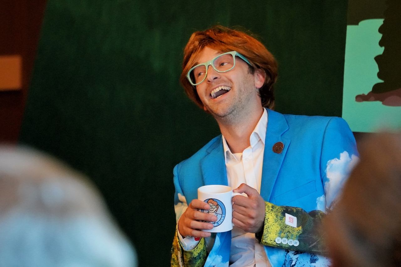 Performer in a bright jacket holding a mug during a relaxed stage moment