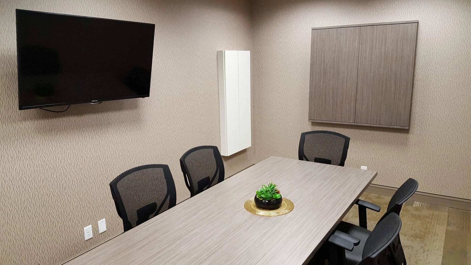 Small meeting room with boardroom table, chairs, and wall-mounted screen.