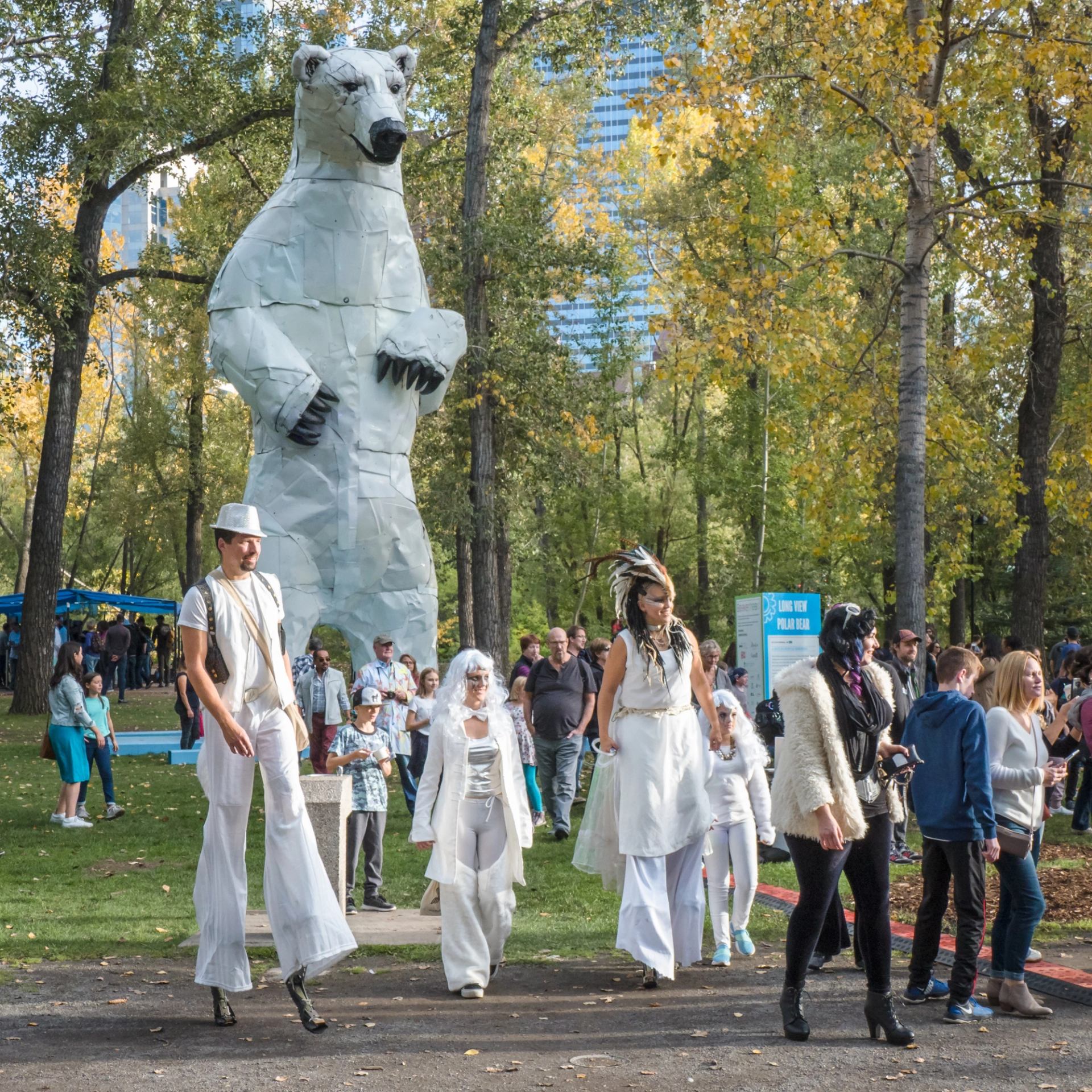 Costumed people walk in front of a giant polar bear statue.